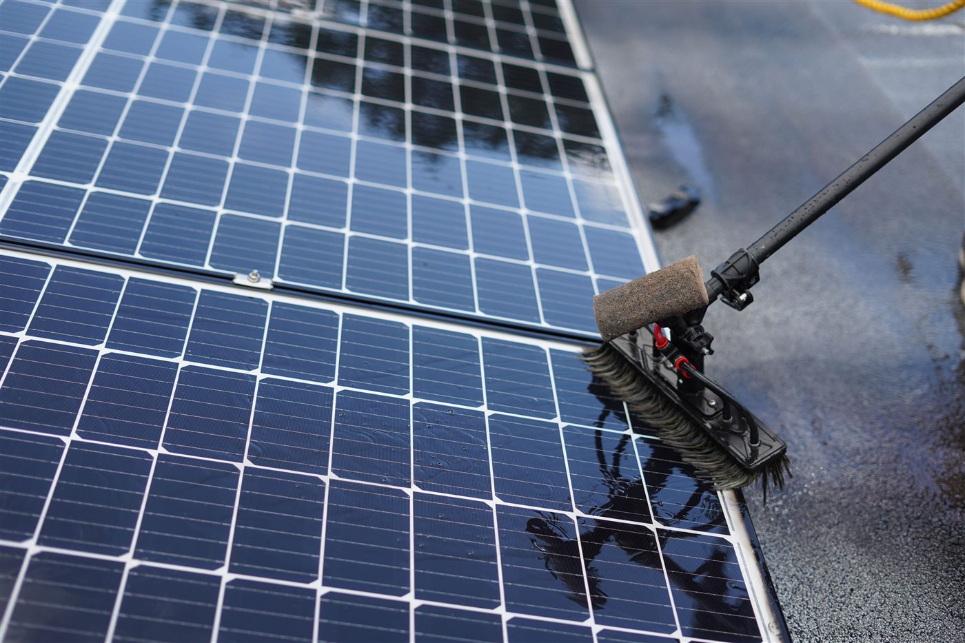 A solar panel being cleaned with a soft brush and water, close-up, water beading on the glass