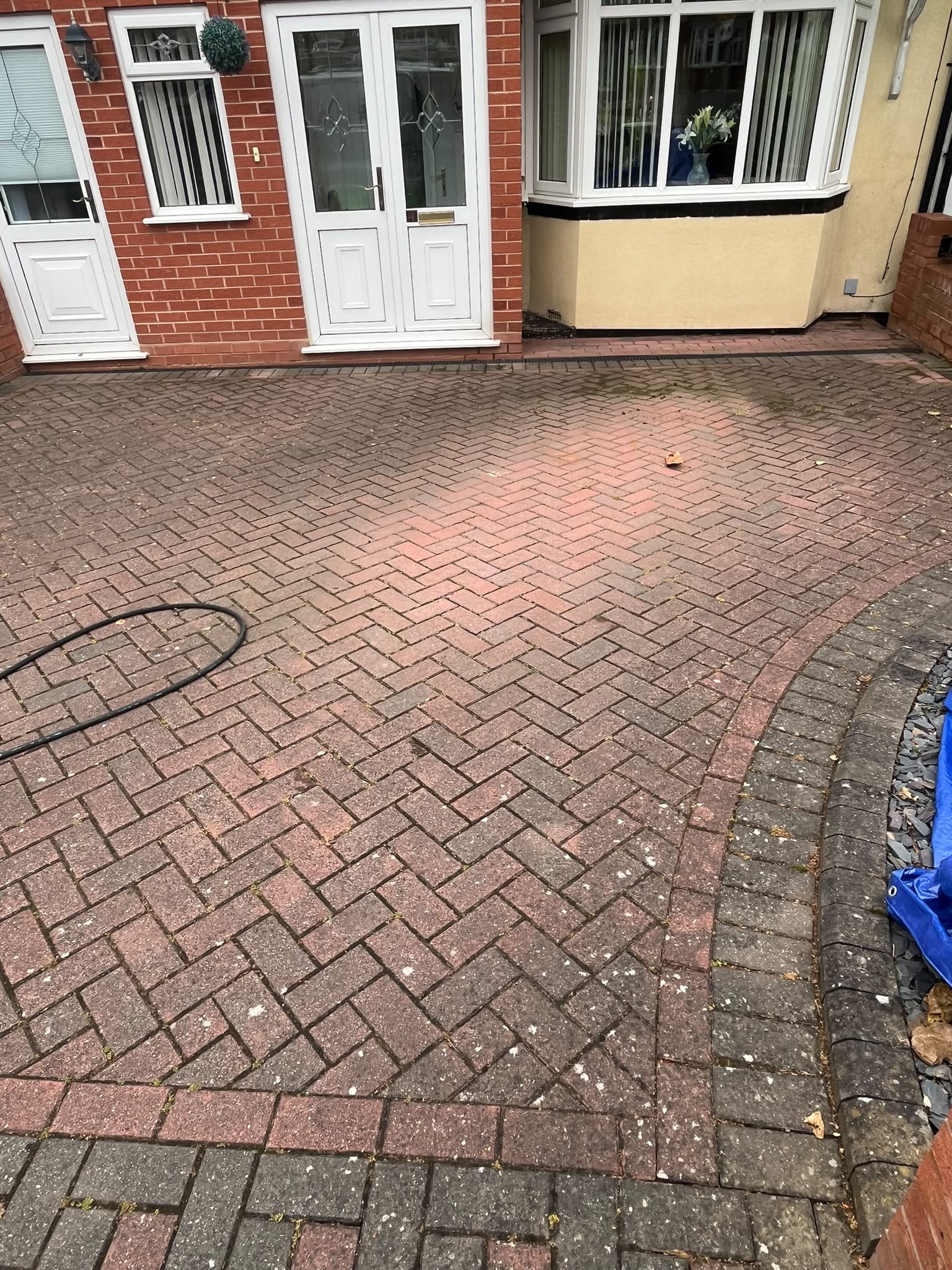 Dirty herringbone block-paving driveway before pressure washing, in front of a red-brick house