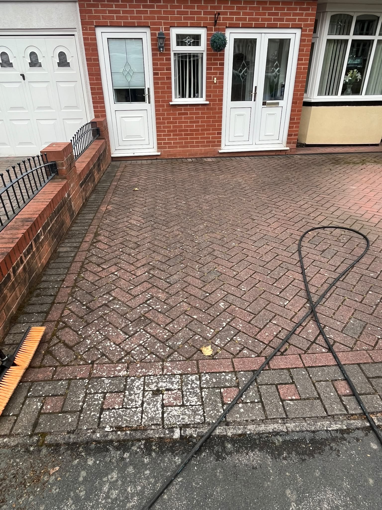 Dirty herringbone block-paving driveway before pressure washing, white garage in the background