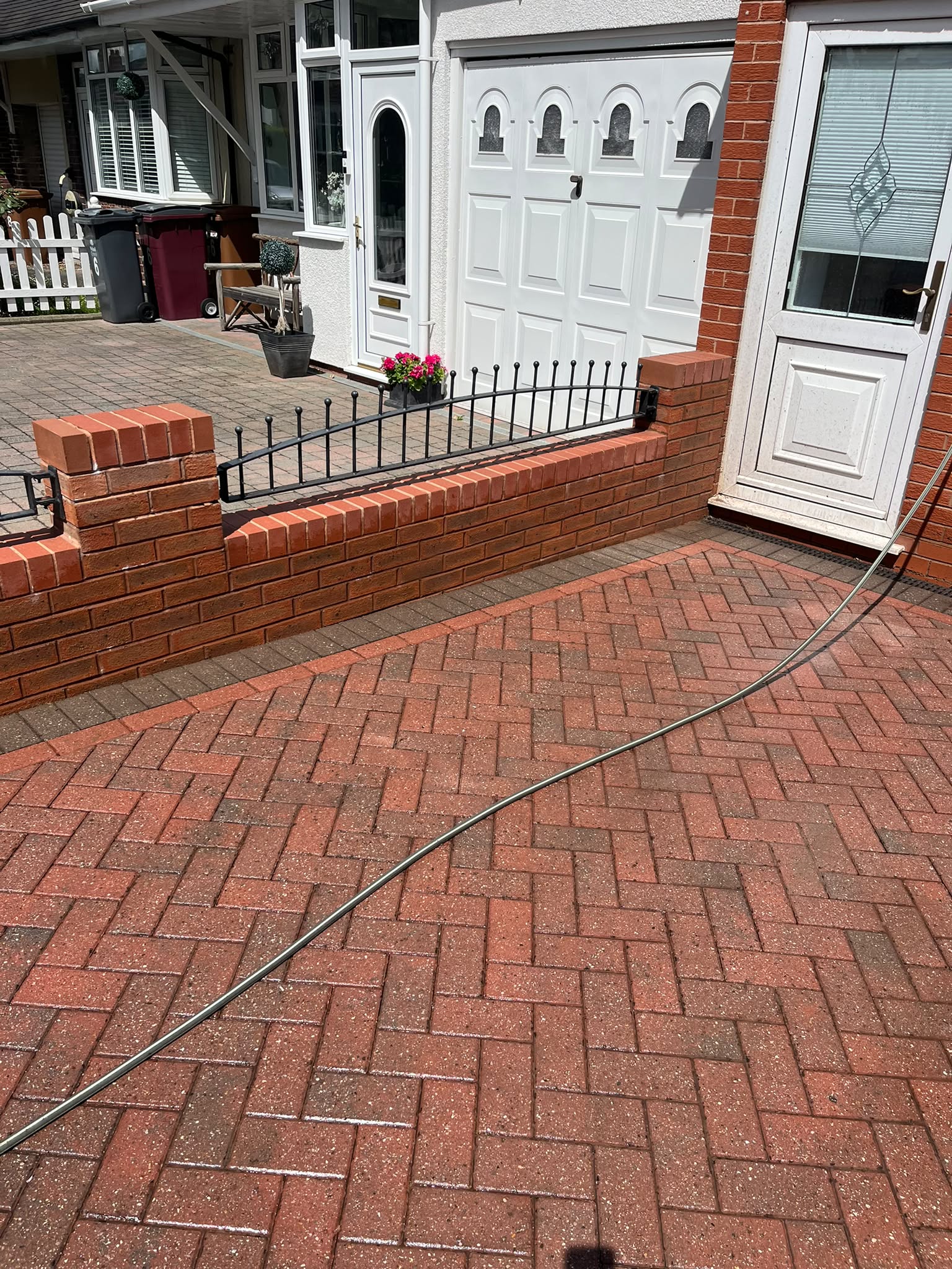 Clean driveway and garden wall corner after pressure washing, with potted plants