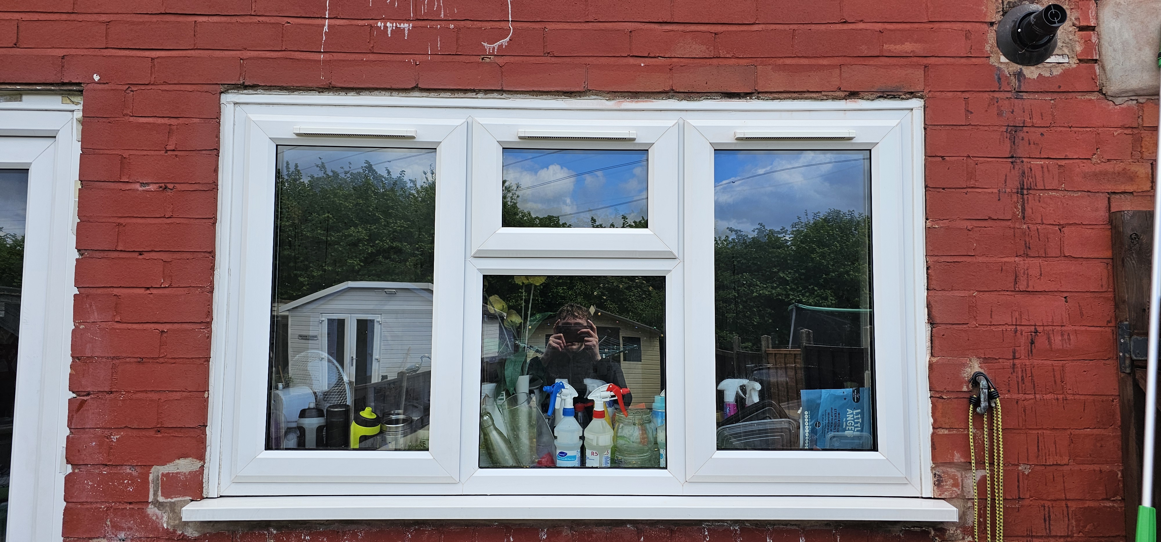 Window cleaner reflected in the glass, with cleaning supplies on the sill